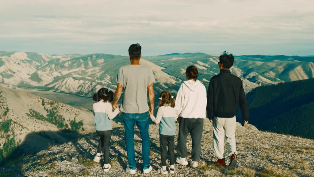 A family stands on a mountain in North Mongolia holding hands and looking out at the spectacular North Mongolian countryside Khasar's North Mongolia Khuvsgul Loop