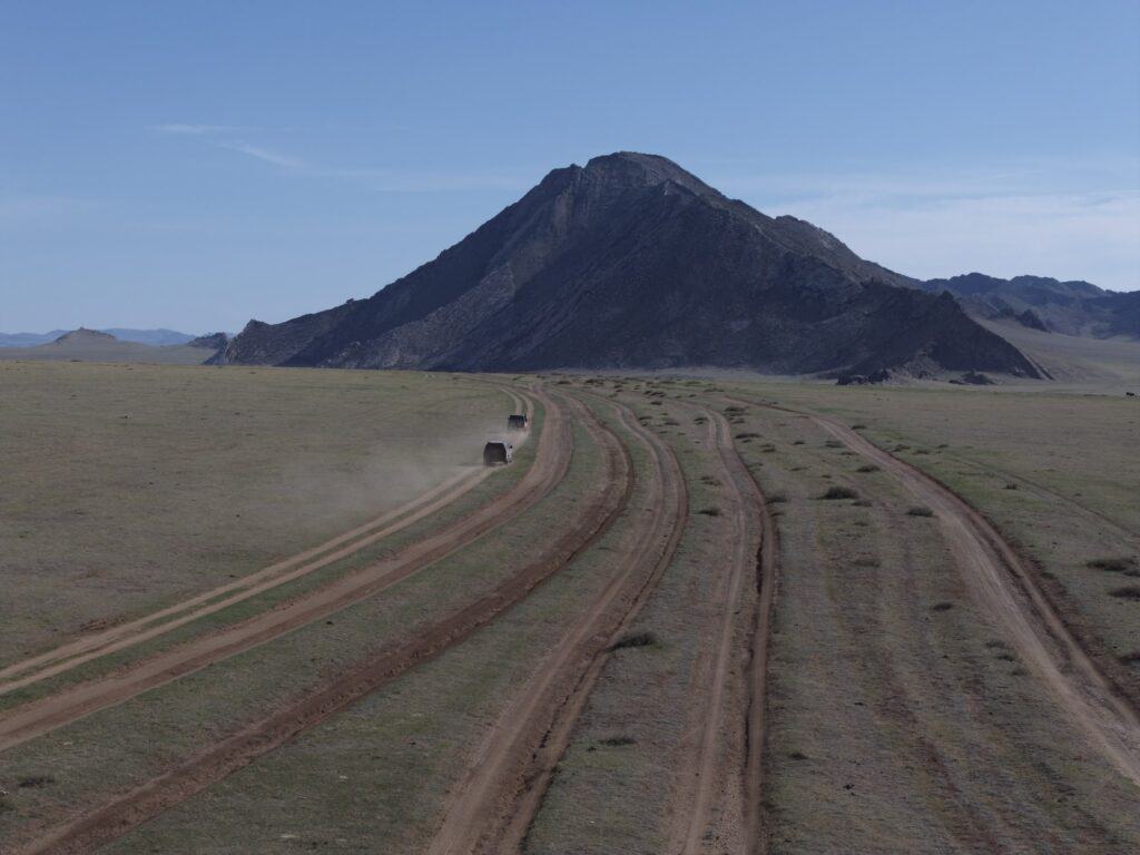A car drives offroad in North Mongolia with a large mountain in the background