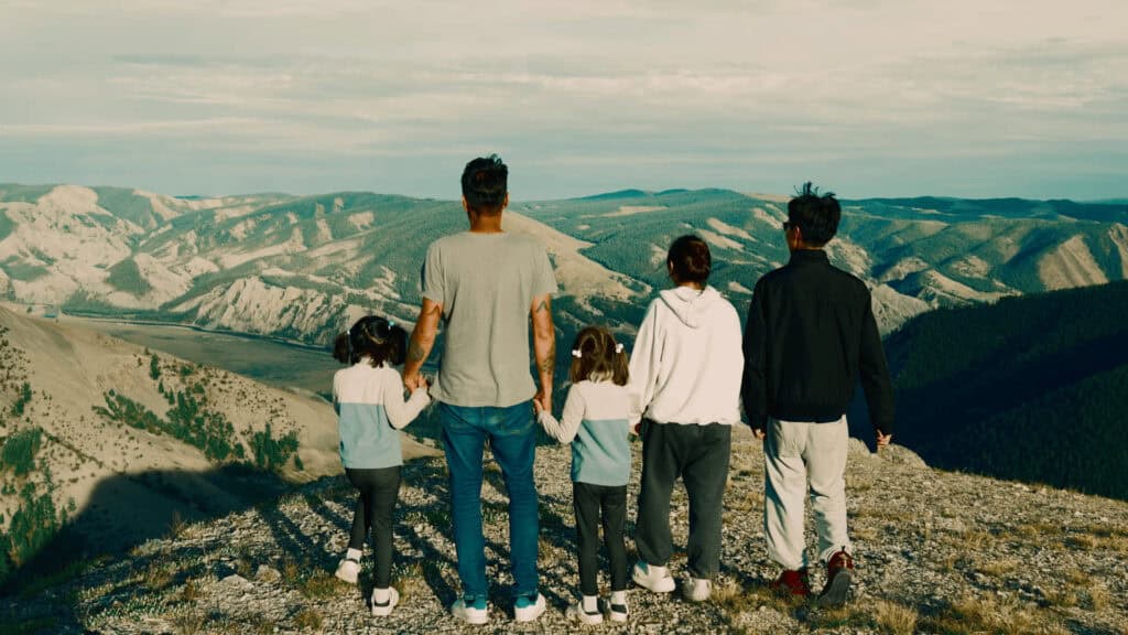 A family stands on a mountain in North Mongolia holding hands and looking out at the spectacular North Mongolian countryside