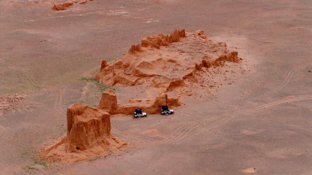 Flaming Cliffs at sunset in Mongolia’s Gobi Desert with vehicles parked nearby.
