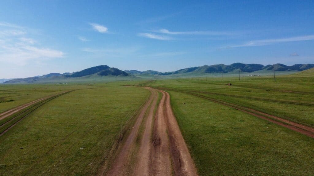 Dirt tracks cut through an endless green field with blue mountains far in the background.