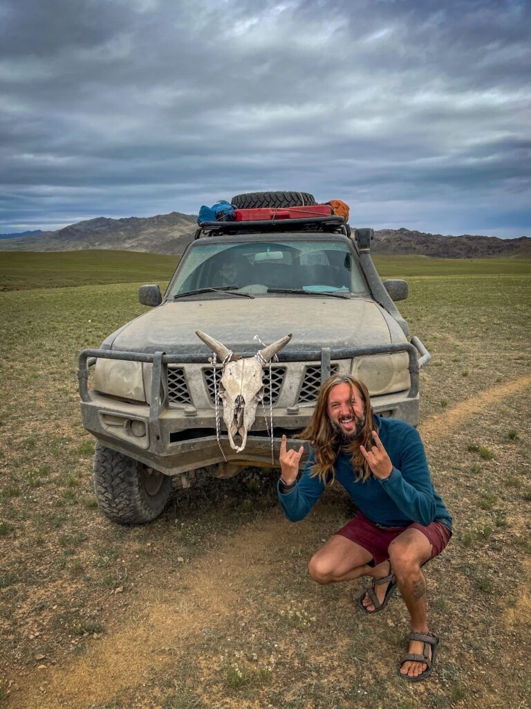 Man on a Bachelor Party in Mongolia poses in front of a 4x4 with a cow skull tied to the front