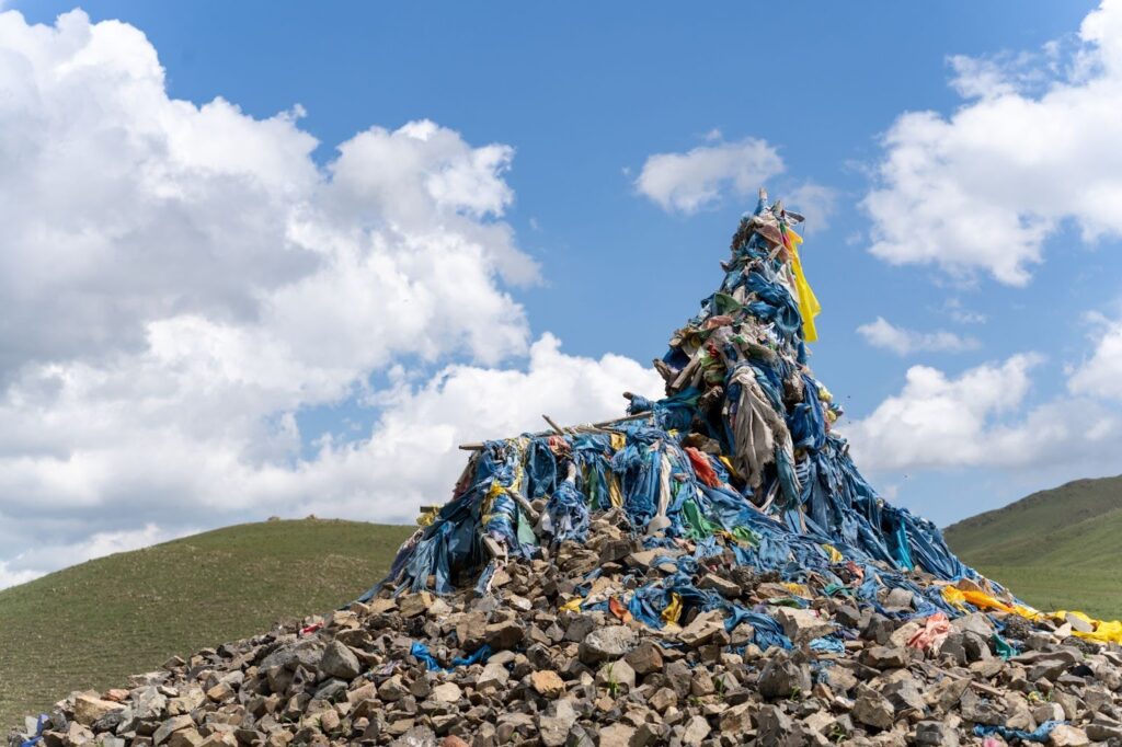 The blue flags of a mongolian prayer pile with green hills in the backgrounds.