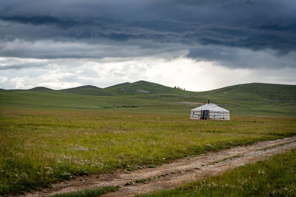 A white ger near a dirt path in a grassy field. The landscape in Mongolia.