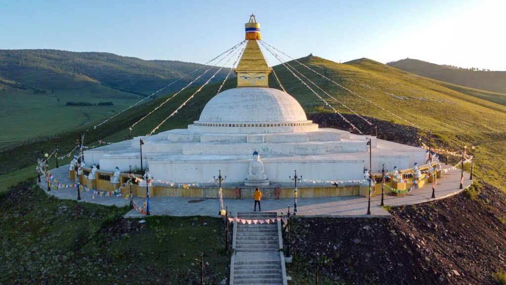 A giant white stupa on a hillside with the morning glow of sunrise.