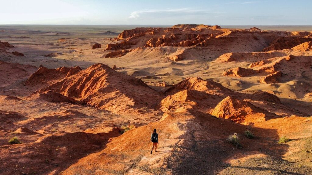 A woman walks on bright orange cliffs on Mongolia's flaming cliffs.