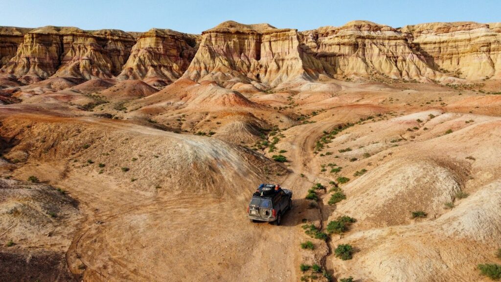 4x4 vehicle on the dirt trails in the Mongolian desert beneath the colorful cliffs of the white stupa.