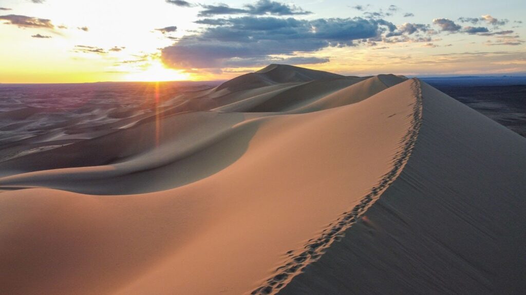 Sunset behind a massive sand dune with footprints on top of it.