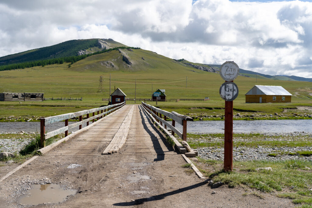 Wooden bridge that goes over a river with Mongolian road signs